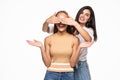 Beautiful woman covering eyes of her friend standing behind and smiling at camera over white background Royalty Free Stock Photo