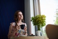 Young woman with cup of coffee in hands sitting at the table near a window in cafe. Coffee break time Royalty Free Stock Photo