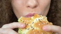 Beautiful woman with curly hair eats a juicy hamburger. closeup