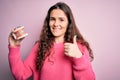 Beautiful woman with curly hair holding plastic teeth with dental braces over pink background happy with big smile doing ok sign, Royalty Free Stock Photo
