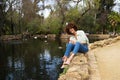 Beautiful woman with curly hair sitting on a duck and swan pond in the park. The woman is happy and holds a red flower in her hand