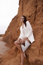 beautiful woman with dark hair in elegant clothes posing on the beach with rocks Royalty Free Stock Photo