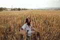 Beautiful woman with dark hair in elegant dress with accessories posing in blooming wheat field