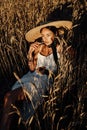 Beautiful woman with dark hair in elegant dress and big straw hat posing among wheat summer field