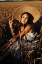 Beautiful woman with dark hair in elegant dress and big straw hat posing among wheat summer field Royalty Free Stock Photo