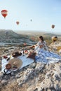 Beautiful woman with dark hair in elegant dress having picnic with fantastic view on valley with air balloons on background