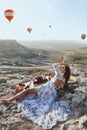 Beautiful woman with dark hair in elegant dress having picnic with fantastic view on valley with air balloons on background