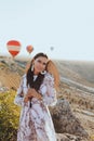 Beautiful woman with dark hair in elegant dress having picnic with fantastic view on valley with air balloons on background