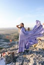 Beautiful woman with dark hair in elegant dress having picnic with fantastic view on valley with air balloons on background