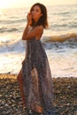 Beautiful woman with dark hair in elegant dress posing on sunset beach Royalty Free Stock Photo