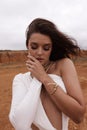 beautiful woman with dark hair in luxurious white dress with accessories posing in desert in Cyprus