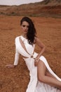 beautiful woman with dark hair in luxurious white dress with accessories posing in desert in Cyprus