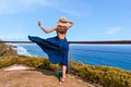 Beautiful woman with dark long hair in elegant blue dress posing in the cliff with ocean view