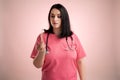 Beautiful woman doctor with stethoscope, wearing pink sctubs is looking at the thermometer Royalty Free Stock Photo