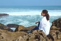 Beautiful woman dreamily looking into the distance, sitting on the cliff by ocean shore, feeling connection with nature Royalty Free Stock Photo