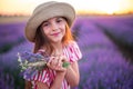 Beautiful woman with dress and hat enjoying color lavender rows in endless blooming field. Girl with flower bouquet