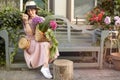 Beautiful woman in a dress with purchases, sits on a bench in the city street. A large basket of vegetables and flowers in the Royalty Free Stock Photo