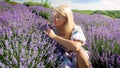 Beautiful young woman in dress sitting in lavender field and smelling flowers Royalty Free Stock Photo