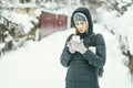 Beautiful woman dressed in a black winter jacket with mobile phone and thermos flask under her arm. Snow landscape Royalty Free Stock Photo