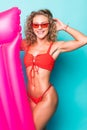 Beautiful young woman dressed in red swimsuit and sunglasses posing with pink inflatable mattress isolated over green background Royalty Free Stock Photo