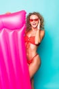 Beautiful young woman dressed in red swimsuit and sunglasses posing with pink inflatable mattress isolated over green background Royalty Free Stock Photo