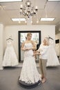 Beautiful woman dressed up as bride with senior employee helping in bridal store