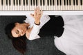 Beautiful woman dressed in a white dress with a black corset lies on the floor near white piano playing on the keys. Place for