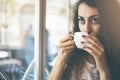 Beautiful woman drinking coffee at cafe. Portrait of young woman in a cafeteria drinking hot cappuccino. Pretty woman with