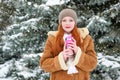 Beautiful woman drinking a hot drink and keep warm on winter outdoor, snowy fir trees in forest, long red hair, wearing a sheepski Royalty Free Stock Photo