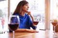 Beautiful woman drinking red wine with friends in cafe, portrait with wine glass near window. Vocation holidays bar concept