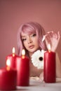 Beautiful woman with dyed pink hair guessing at flower in hand at table with candles. Pink beauty hair on head of woman fortune