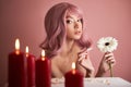 Beautiful woman with dyed pink hair guessing at flower in hand at table with candles. Pink beauty hair on head of woman fortune