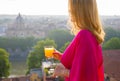 Woman in early morning with glass of fresh orange juice standing on terrace overlooking city