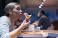 Beautiful woman eating pizza and drinking cola while sitting inside expres restaurant late at night Royalty Free Stock Photo