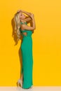 Beautiful Woman In Elegant Green Long Dress Is Standing Against Yellow Wall. Side View Royalty Free Stock Photo