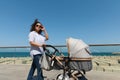 Beautiful woman enjoying a promenade along Atlantic seacoast in warm sunny day, pushing a stroller with her newborn baby Royalty Free Stock Photo