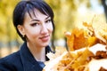 Beautiful woman face closeup with handful of yellow leaves in autumn outdoor, trees on background, fall season