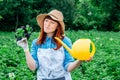 Beautiful woman farmer holds a bunch of basil and watering garden in a straw hat and surrounded by the many plants in her Royalty Free Stock Photo