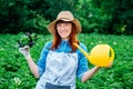 Beautiful woman farmer holds a bunch of basil and watering garden in a straw hat and surrounded by the many plants in her Royalty Free Stock Photo