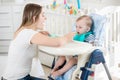 Beautiful woman feeding her baby boy in highchair at living room Royalty Free Stock Photo