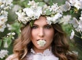 Beautiful woman with a flower wreath under a blooming tree. A young girl with a flower in her mouth against the background of Royalty Free Stock Photo