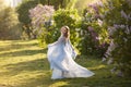 Beautiful woman in flying airy blue dress in blooming lilac garden. Royalty Free Stock Photo