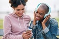 beautiful woman friends using smartphone listening to music on mobile phone wearing headphones hanging out together Royalty Free Stock Photo