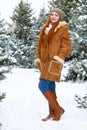 Beautiful woman full length on winter outdoor, snowy fir trees in forest, long red hair, wearing a sheepskin coat Royalty Free Stock Photo