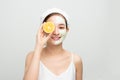 Beautiful woman is getting facial clay mask and holding orange pieces on white background. Beauty, body care and spa concept Royalty Free Stock Photo