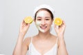 Beautiful woman is getting facial clay mask and holding orange pieces on white background. Beauty, body care and spa concept Royalty Free Stock Photo