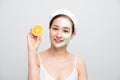 Beautiful woman is getting facial clay mask and holding orange pieces on white background. Beauty, body care and spa concept Royalty Free Stock Photo