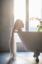 A beautiful woman with gorgeous long blond hair is relaxing in the bath. Silhouette of a woman in profile lying in the bathroom Royalty Free Stock Photo