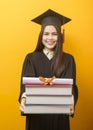 Beautiful woman in graduation gown is holding books and certificate on yellow background Royalty Free Stock Photo