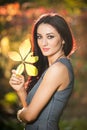 Beautiful woman in gray posing in autumnal park. Young brunette woman holding a leaf and spending time in autumn Royalty Free Stock Photo